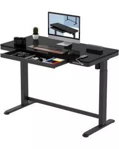 FlexiSpot black electric standing desk with tempered glass top open drawer and monitor setup on white background