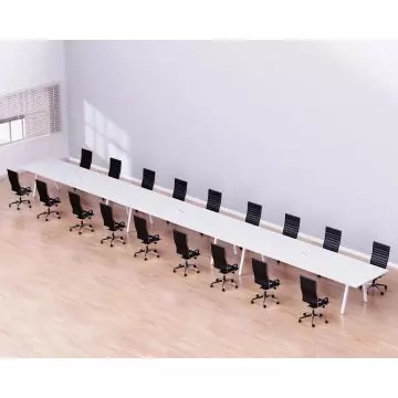 Long white conference table with multiple black office chairs in a spacious  well-lit room with wooden flooring.
