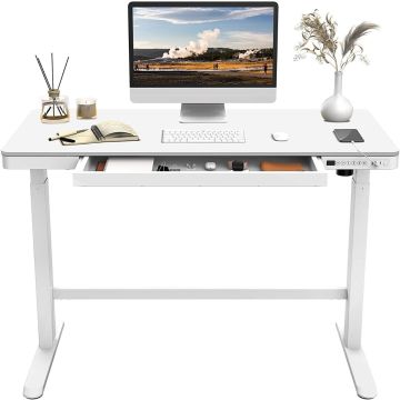 White adjustable standing desk with a built-in drawer  featuring a computer setup  notebook  reed diffuser  candle  and vase with dried flowers.