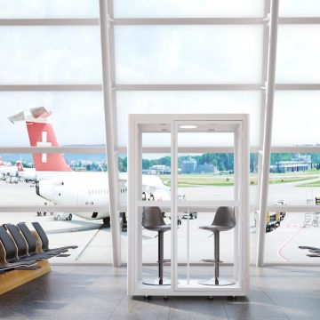 White framed glass phone pod with two stools in an airport lounge