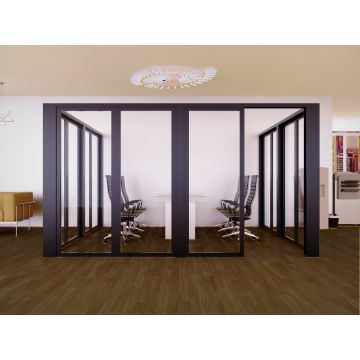 Modern glass-walled office cubicle with sleek black-framed sliding doors  containing ergonomic black office chairs around a white table on wooden flooring.