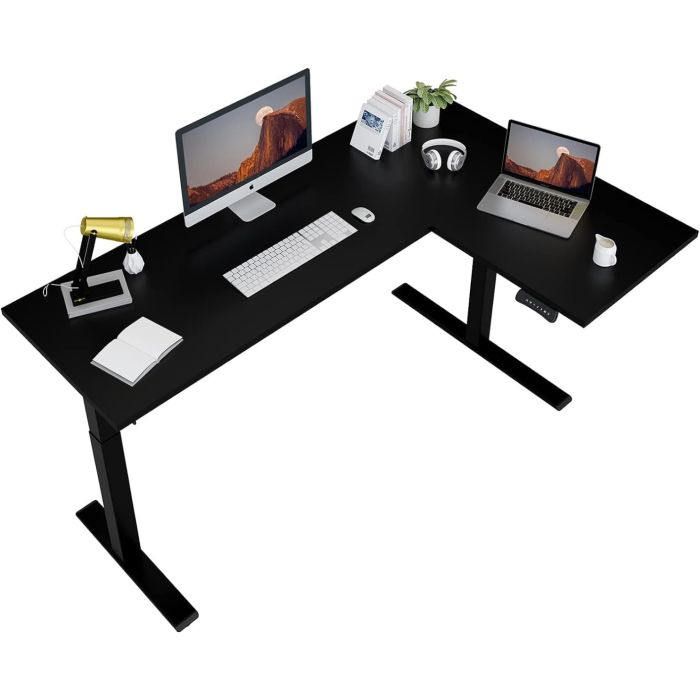 Black L-shaped standing desk with dual monitors  keyboard  lamp  notebook  headphones  books  plant  and coffee cup.